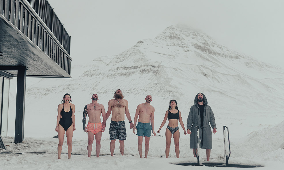 group of people engage in cold plunge in front of snow covered mountain in iceland