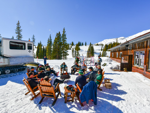 skiers sit around the fire next to the snow cat